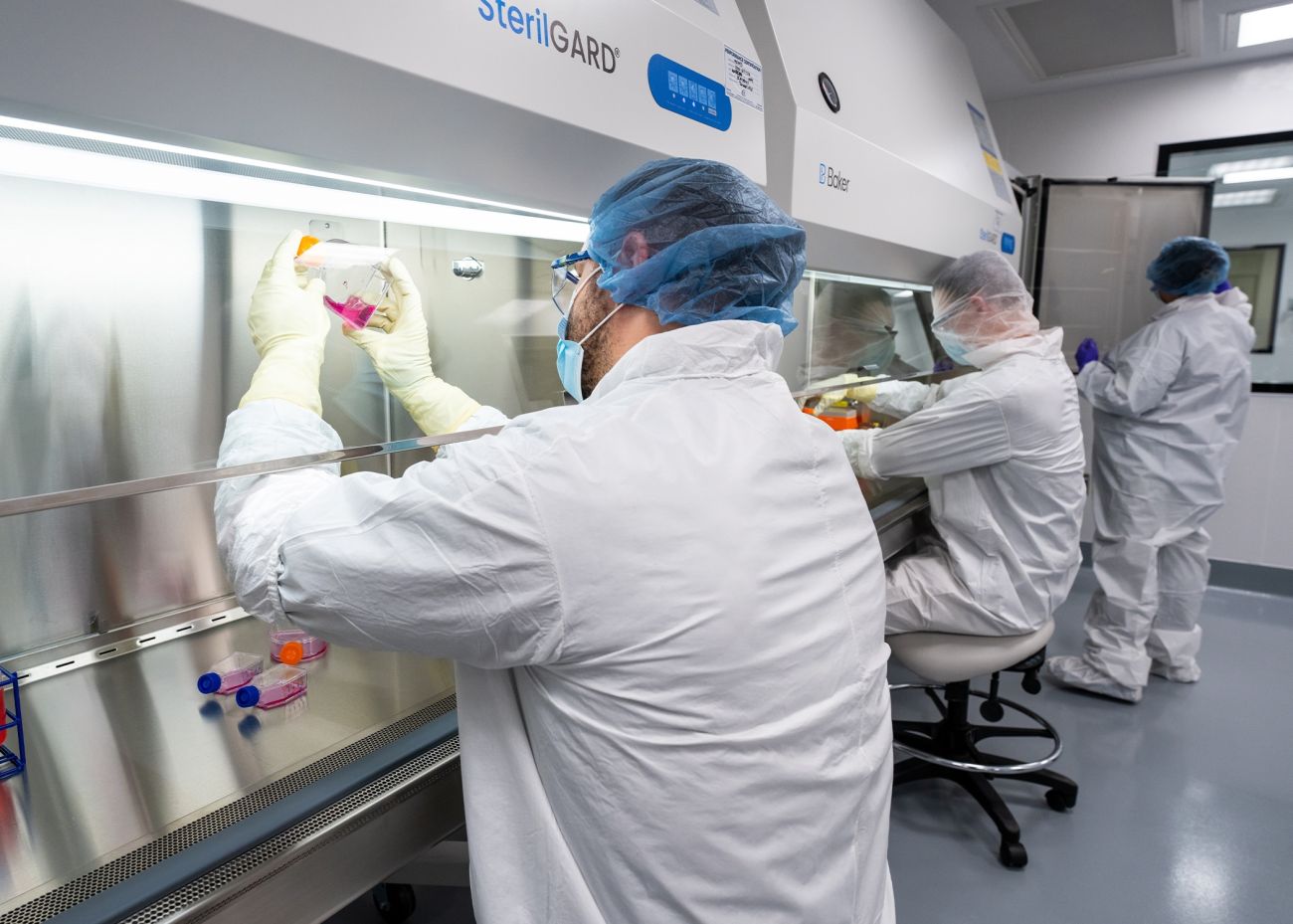 Scientists in white coats and protective gear work in lab