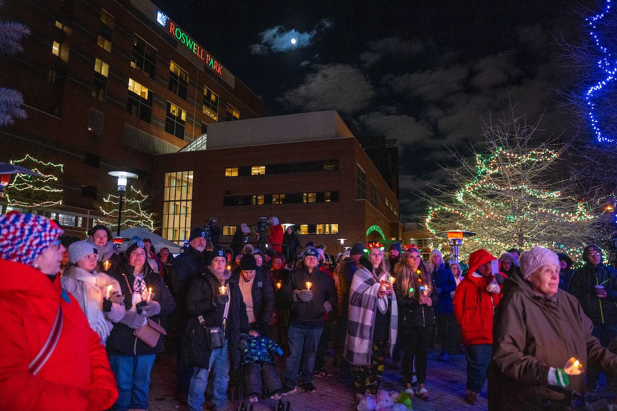 A crowd of people gather outdoors holding candles