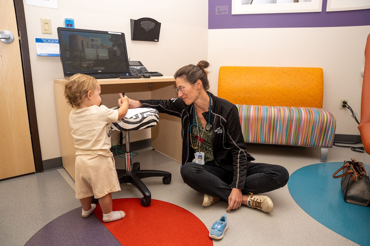 Dr. Katie Carlberg sits on the floor and interacts with a pediatric patient