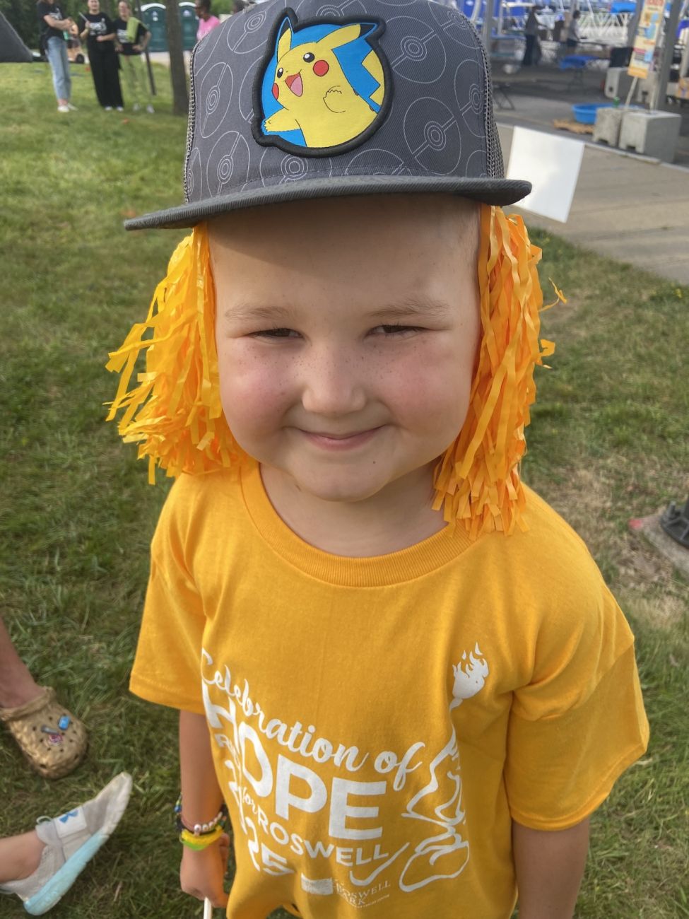 A young cancer patient standing outdoors in a yellow shirt