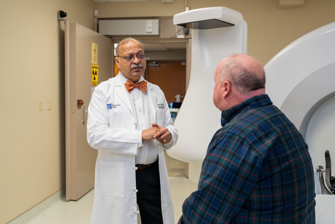 A doctor speaks to their patient in front of a radiation machine to treat cancer.