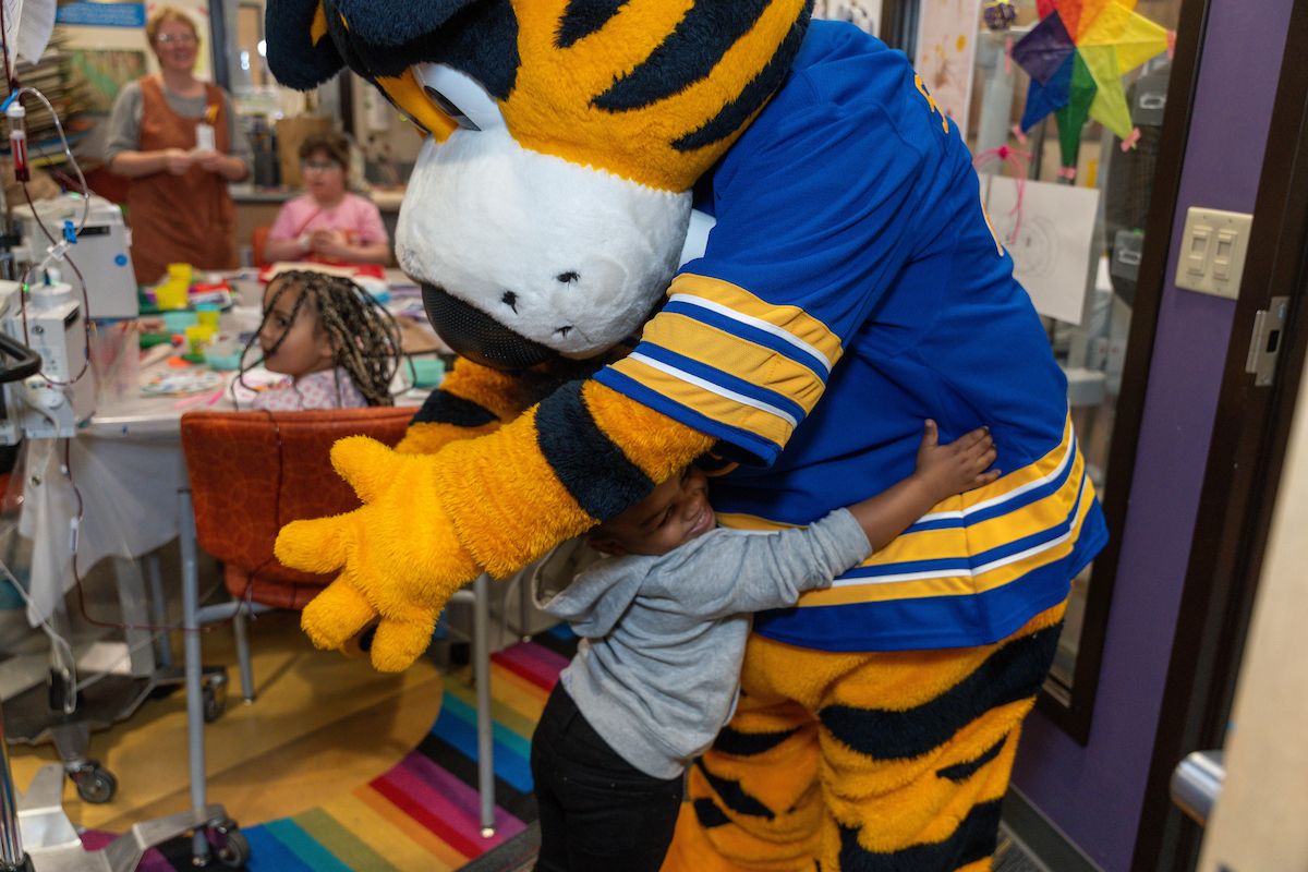 A mascot hugs a young girl in the hospital