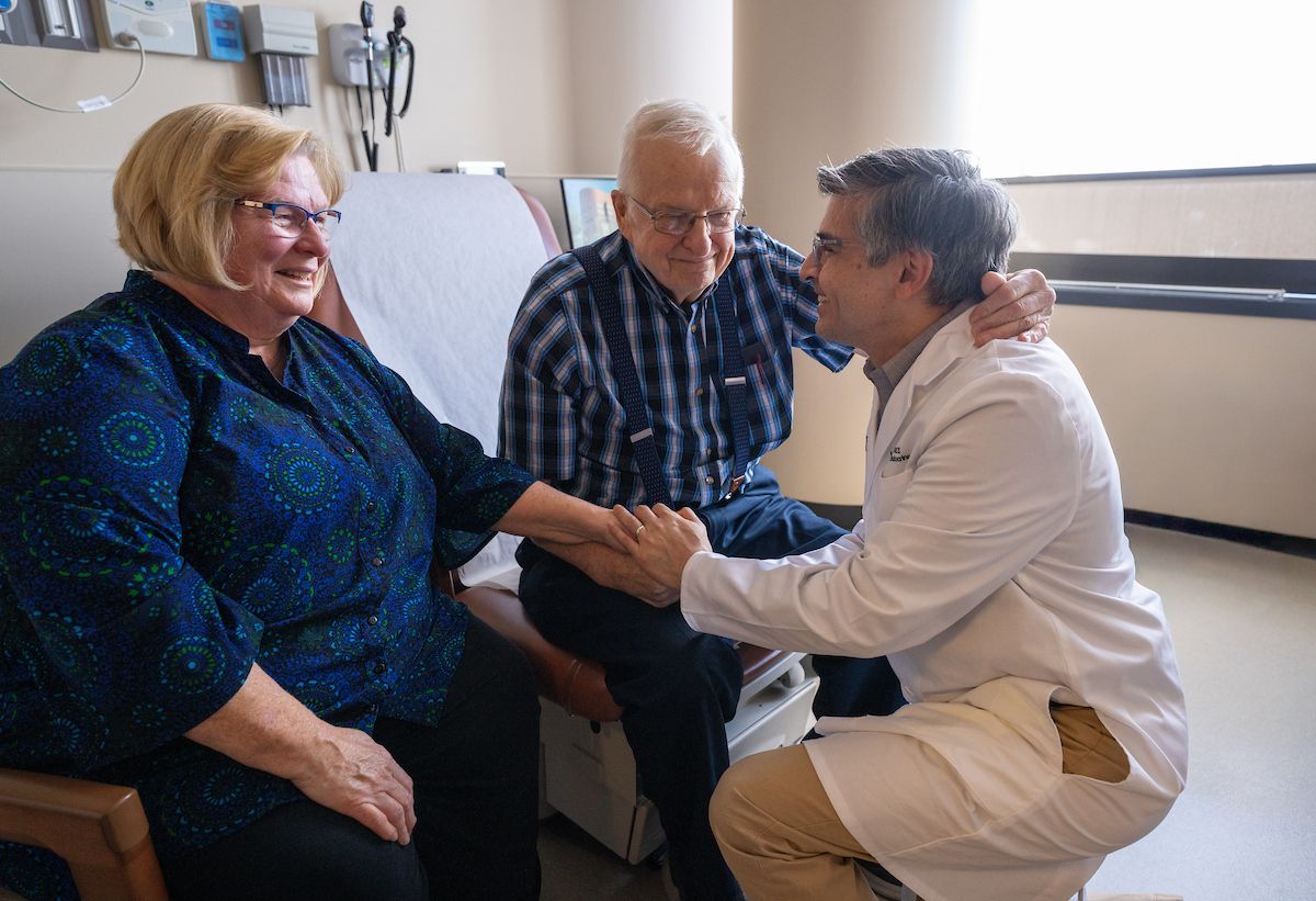 Dr. Mashaal Dhir takes a knee as he's embraced by a patient in clinic