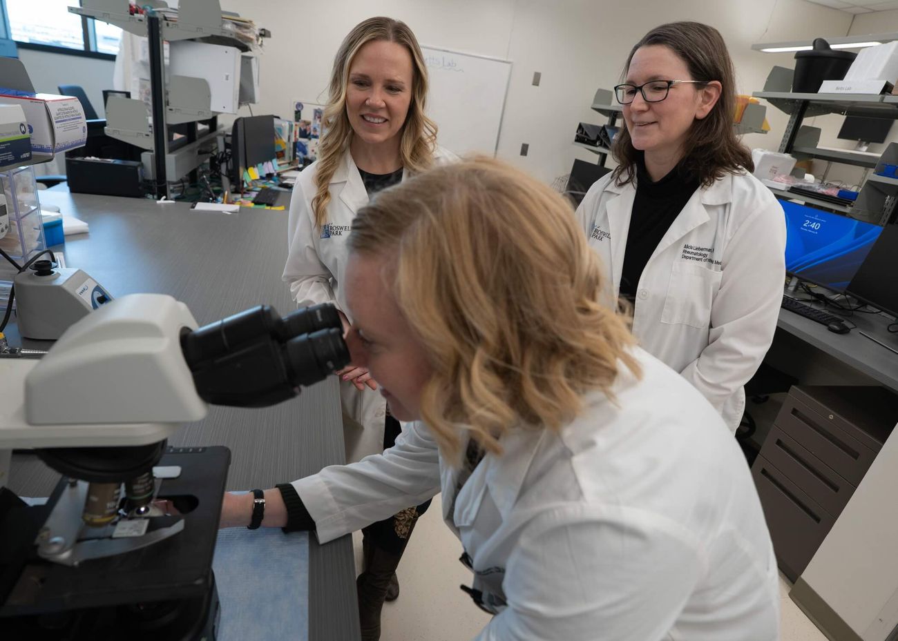 Two doctors look on as another doctor uses a microscope