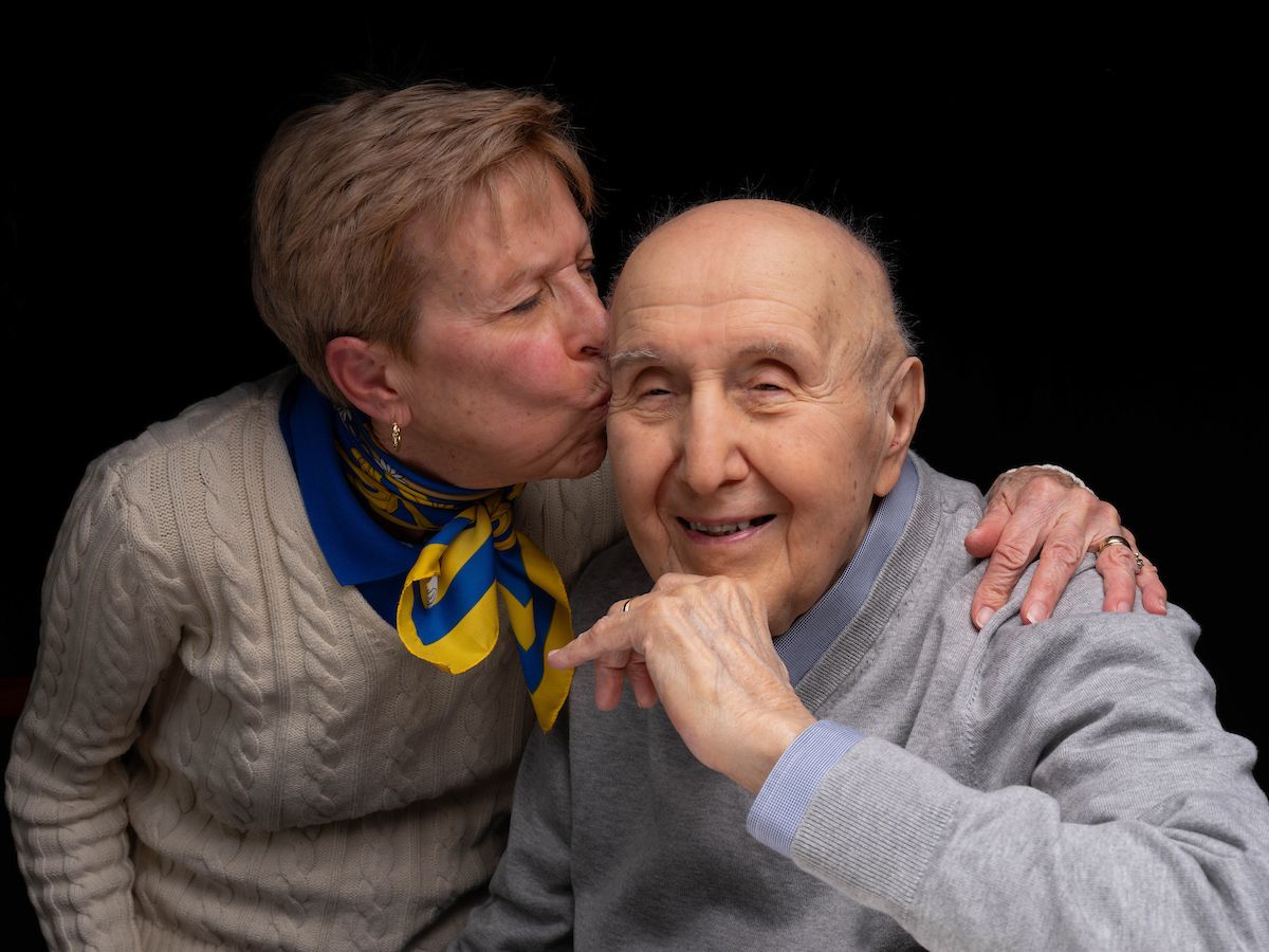 A woman leans in to place a kiss on the forehead of her husband. 