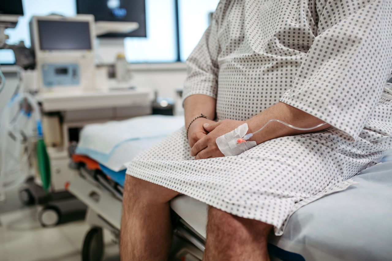 Torso of a man in a hospital gown sitting on a medical bed