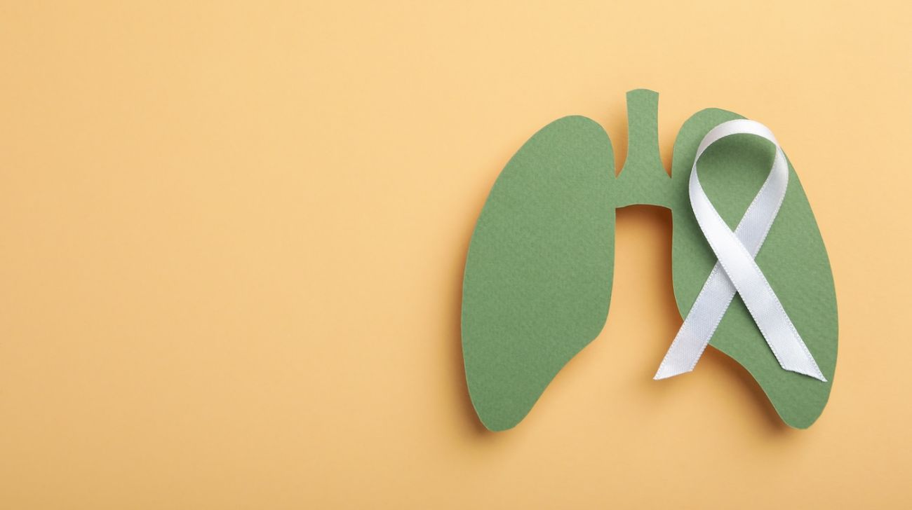 A cut out of a drawing of lungs sits on an orange background with a cancer ribbon laid overtop 