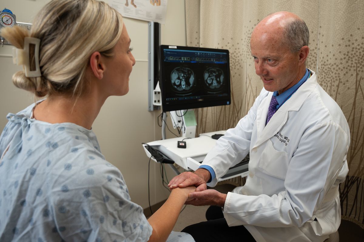 Dr. Gary Mann sits in a clinic room with a patient holding her hand