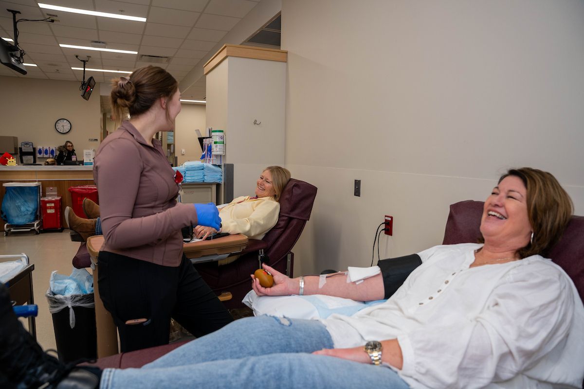 Two women sit next to each other in the Donor Center as they donate blood