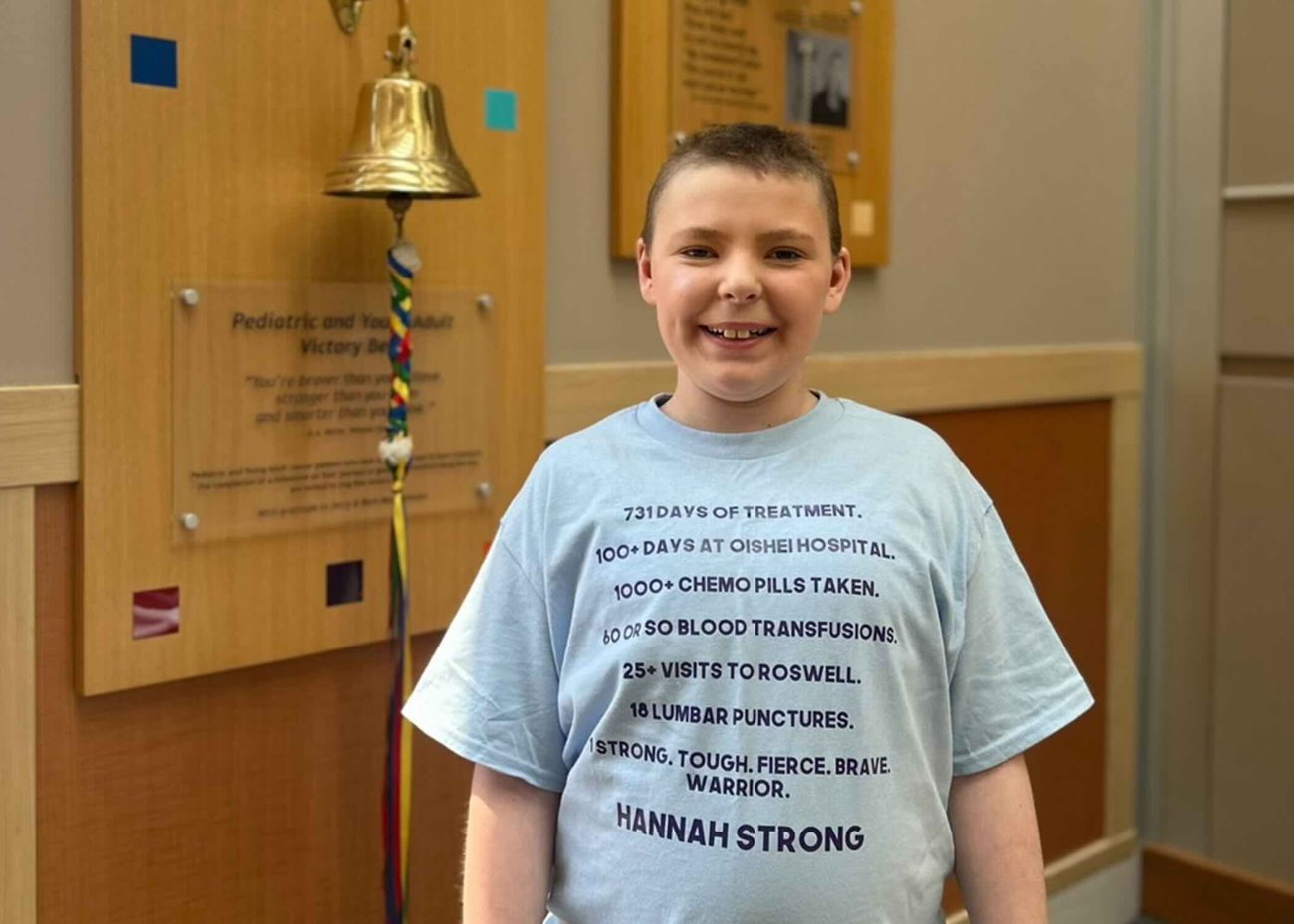 Child cancer patient stands in front of victory bell