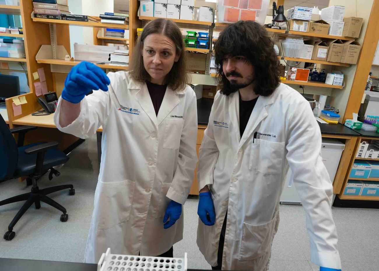 A man and woman in lab coats look at a vial