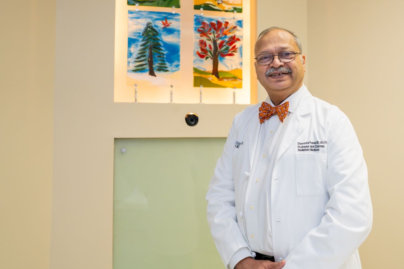A doctor in a white coat stands in front of a painting