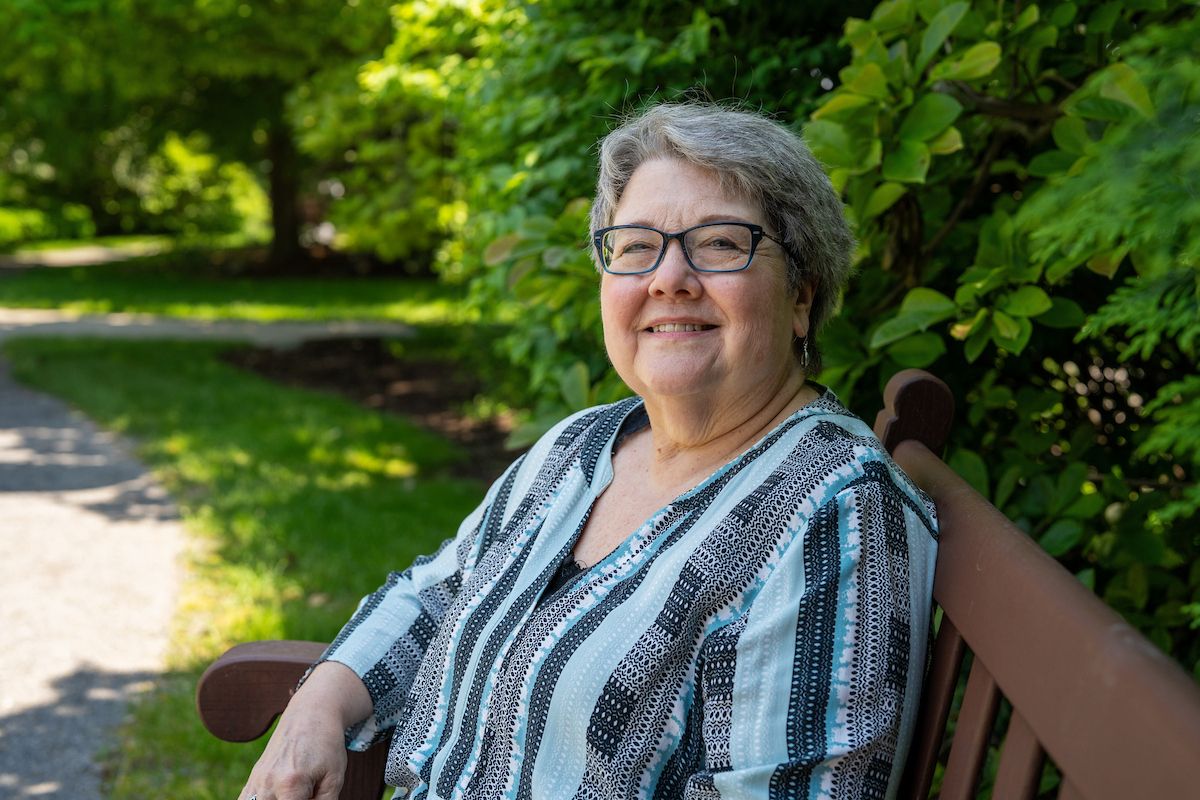Senior citizen sits on bench in Kaminski park and smiles at the camera