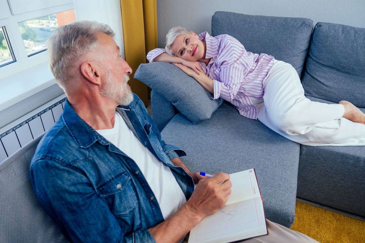 Man writing in book as woman lies on sofa