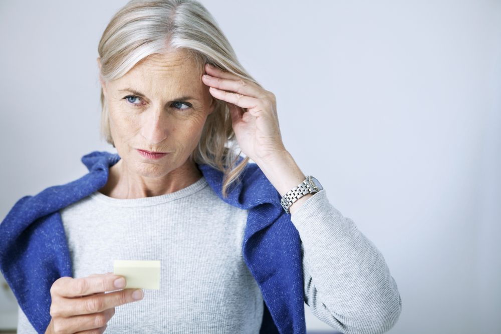 Woman looking at a small piece of paper and putting her hand to her temple