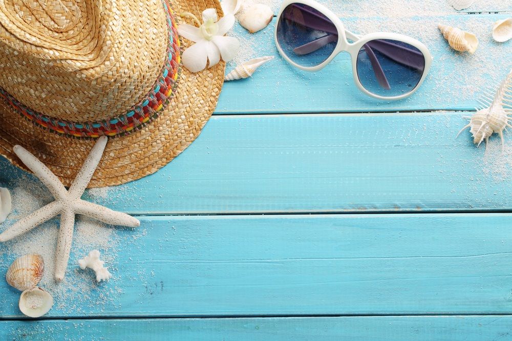 Sunglasses, sun hat, and seashells on a light blue background