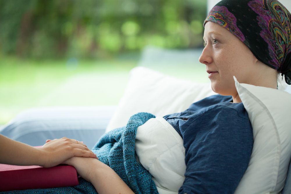 Cancer patient reclining on pillows and holding hands with another person