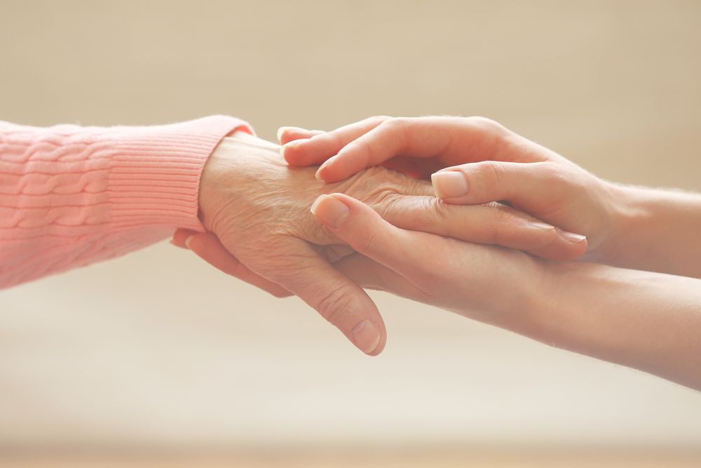 Person with younger hands holding an elderly person's hand