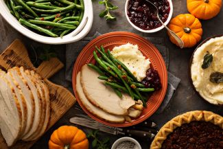 Holiday foods on a table, including turkey, green beans, mashed potatoes and pecan pie