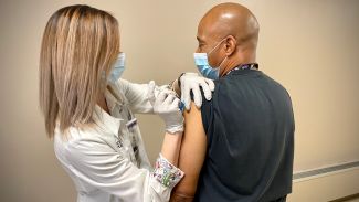 Dwayne Smith, right, a phlebotomist at Roswell Park Comprehensive Cancer Center, receives his first dose of a COVID-19 vaccine. 