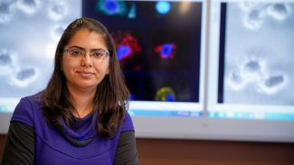 Woman scientist standing in front of a colorful image of cells