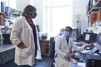 Scientist in white lab coat speaks with two members of her lab