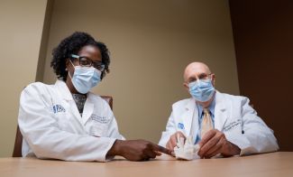 Two physicians point to a model showing the inside of a woman's neck