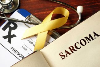 Book with a page titled "sarcoma" placed near a cancer awareness ribbon and stethoscope