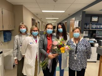 Four women wearing surgical masks stand around a woman in the center, holding flowers and being recognized as Roswell Park's Nurse of the Month for September.