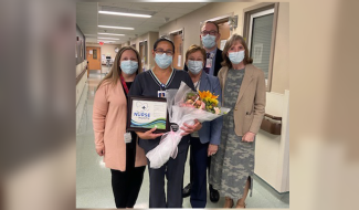 Cindy Latimore, second from left, holds a bouquet of flowers and a certificate, given to her for being named Nurse of the Month for May. She is standing in a hallway with other members of the Roswell Park staff, including President and CEO Candace S. Johnson. 