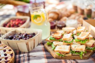 A picnic with sandwiches, pie, berries and a glass of lemonade on a striped blanket.