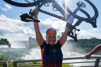 Cyclist raising her arms in front of Niagara Falls.