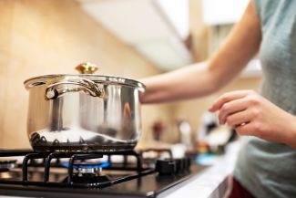 Person cooking in a metal pot on a stove - stock