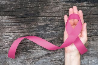 pink breast cancer ribbon on a hand with wood background
