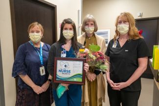Alli Courtney, second from left, holds flowers and a certificate declaring she is Nurse of the Month for December. Three other women stand in a hall with her.