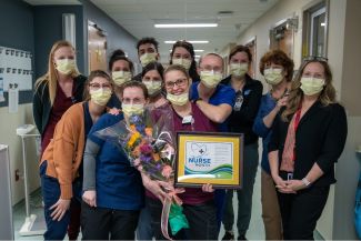 Jen Boehm, middle, is surrounded by her fellow nurses. They are standing in a hallway wearing face masks. 