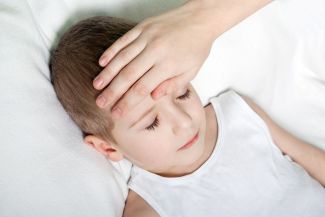 Child laying in bed with someone taking their temperature